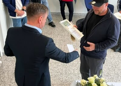 Ein Mann übergibt einem Mitarbeitenden eine Urkunde.