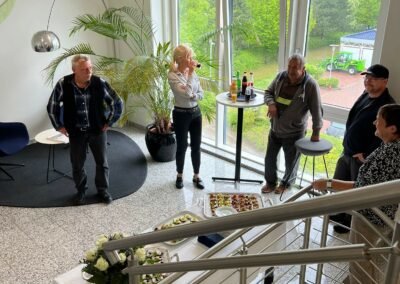 Mehrere Personen (Frauen und Männer) die in einem Treppenhaus stehen. Im Treppenhaus ist ein Tisch mit einem Buffet aufgebaut.