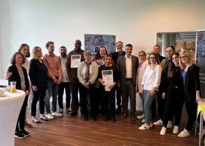 Eine Gruppe von Menschen in einem feierlichen Rahmen. Drei Leute halten eine Urkunde in der Hand.