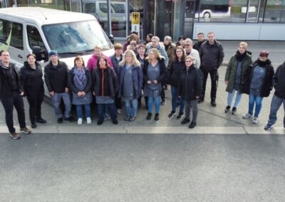 Ein großes Team von Reinigungskräften. Sie alle stehen vor einem Gebäude. Dahinter ist ein Firmenfahrzeug zu sehen. Sie sehen alle freundlich in die Kamera.