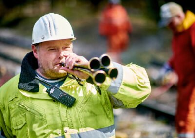 Ein Sicherungsposten der am Gleisbett steht und in ein Horn bläst, das somit ein Warnsignal abgibt für jene Leute die am Gleis arbeiten.