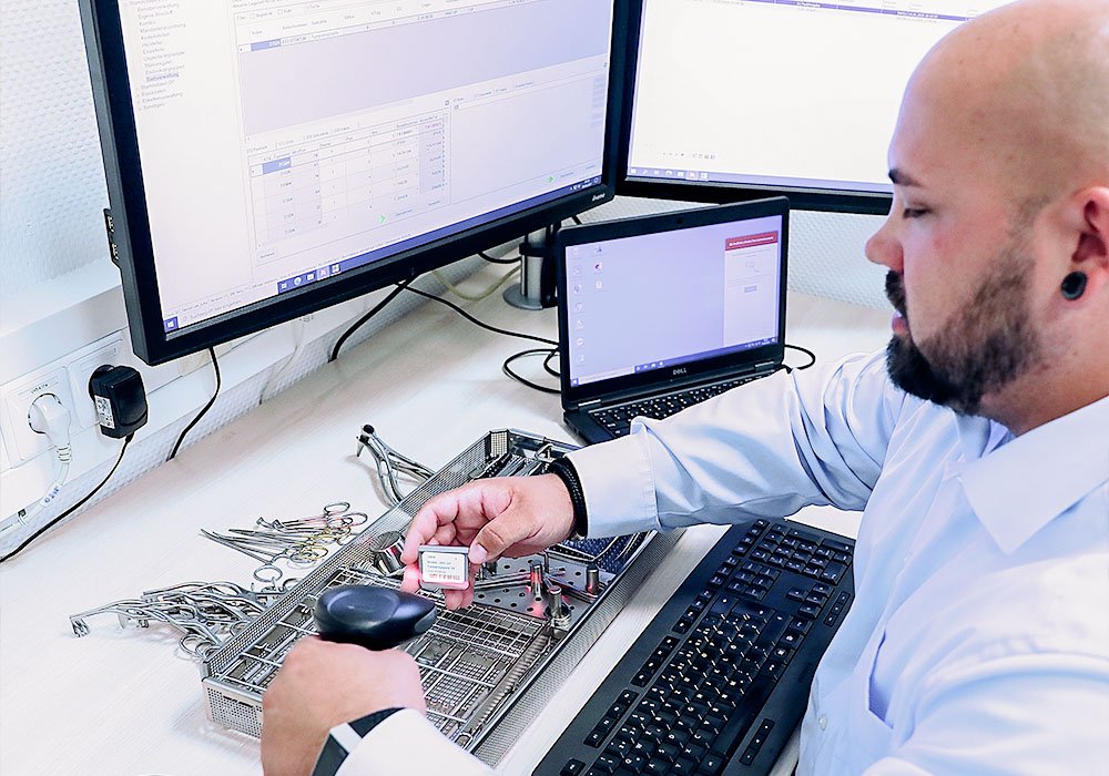 Ein junger Mann in der Sterilgutversorgung eines Krankenhauses. Er sitzt vor einem Computer und scannt das Sterilgut.